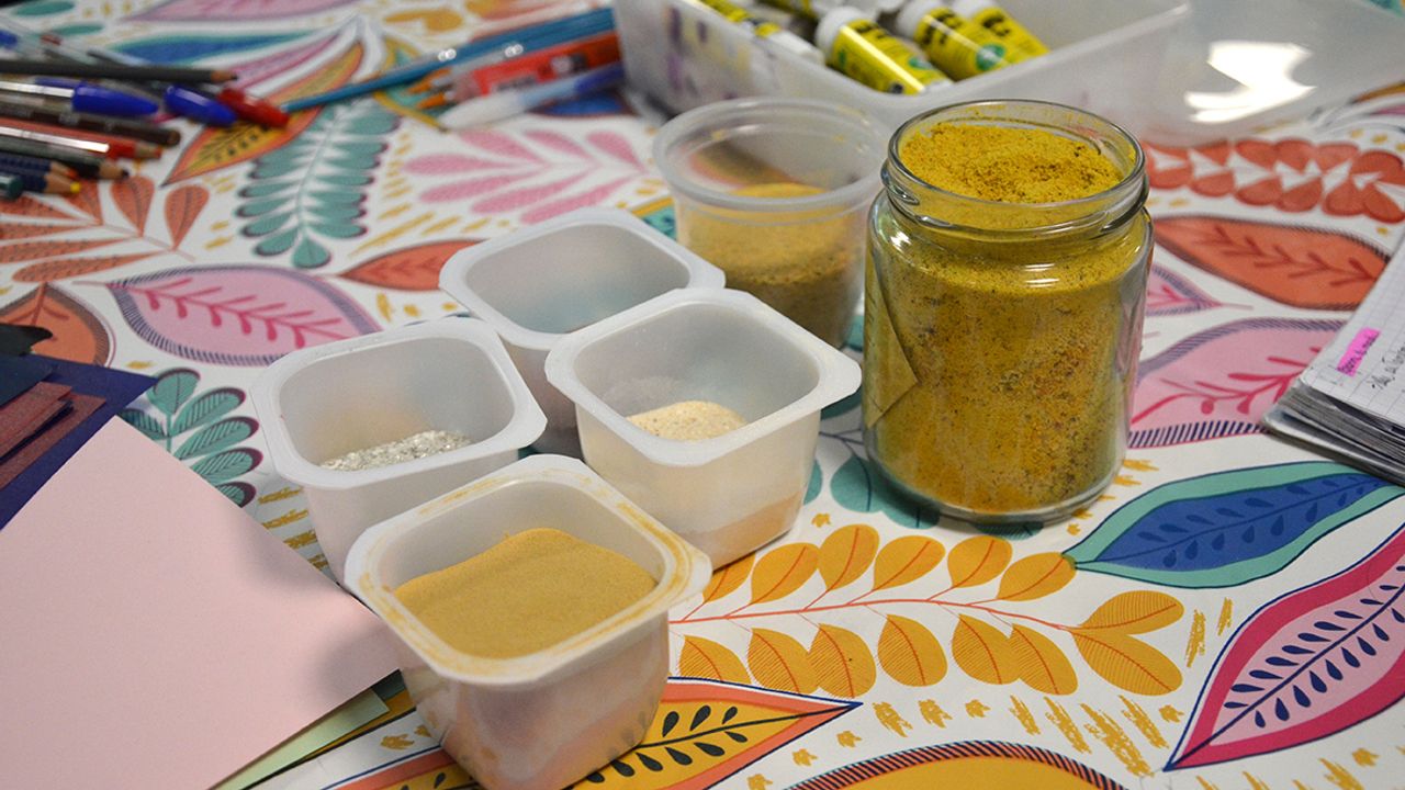 De petits pots remplis de pigments minéraux et des colles sont posés sur une table.