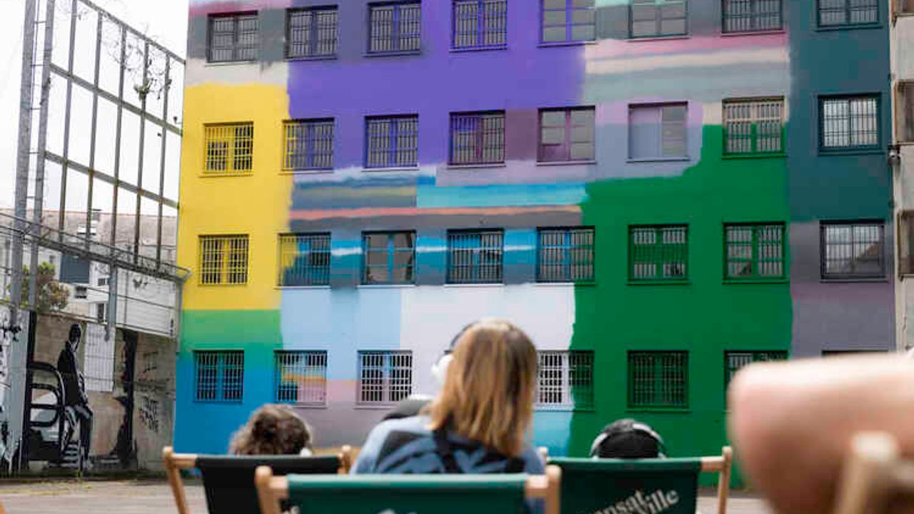 Devant un mur coloré, des personnes écoutent un récit sur des transats