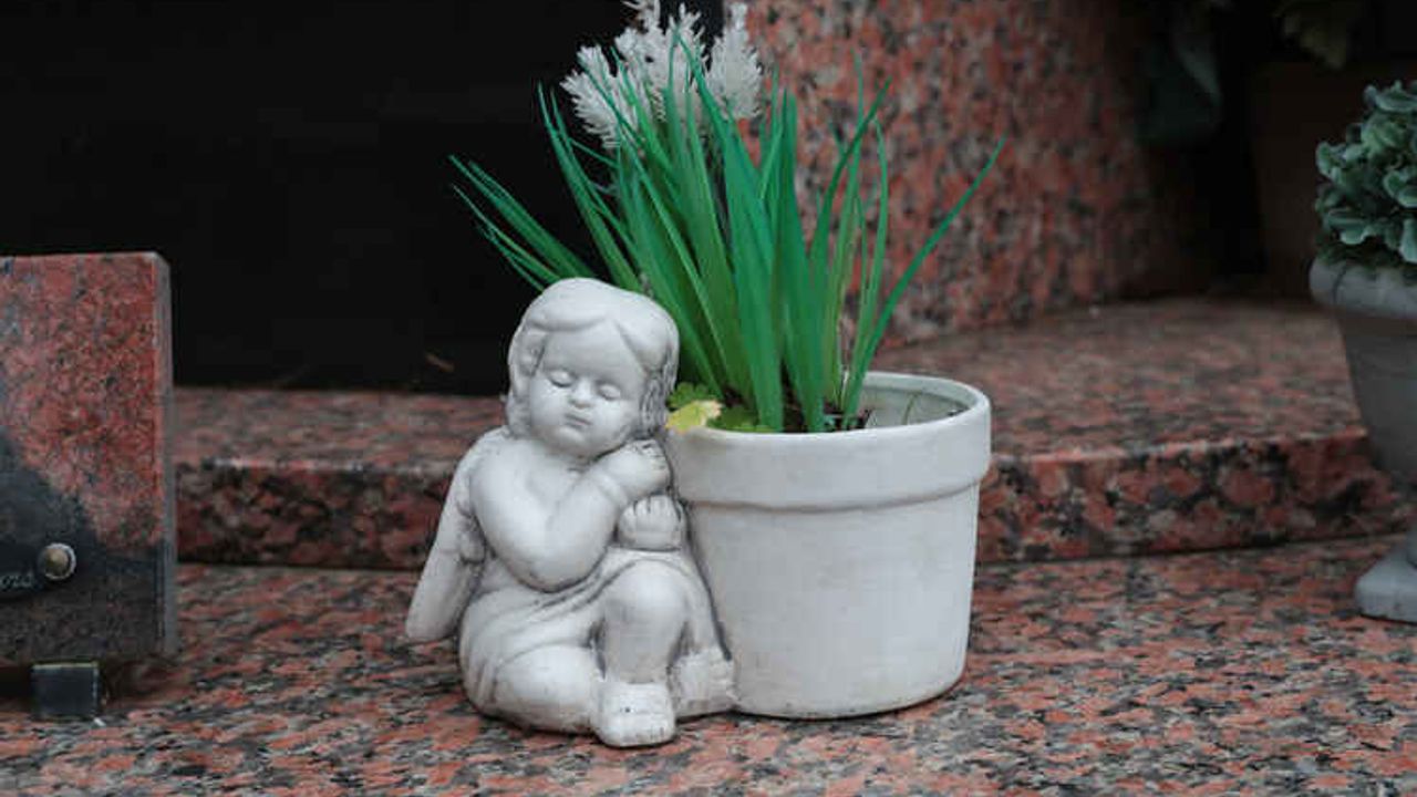 Vue sur un pot de fleurs en céramique blanc figurant un angelot, posé sur une tombe dans un cimetière.