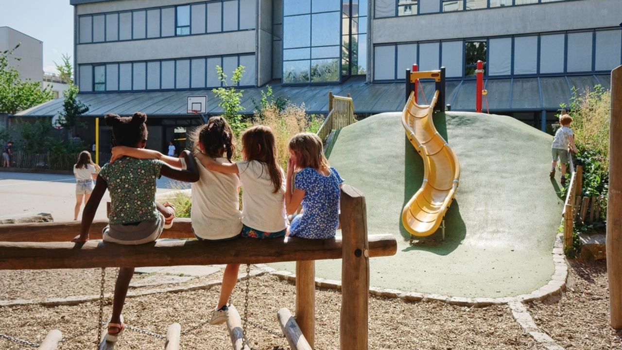 Des enfants jouent dans une cour de récréation végétalisée.