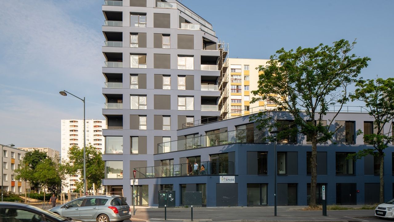 Vue du bâtiment Osmoz, immeuble avec deux étages à droite et huit étages au centre, depuis l'autre côté de l'avenue des Pays-Bas. Sur l'avenue circulent deux voitures, une dans chaque sens.