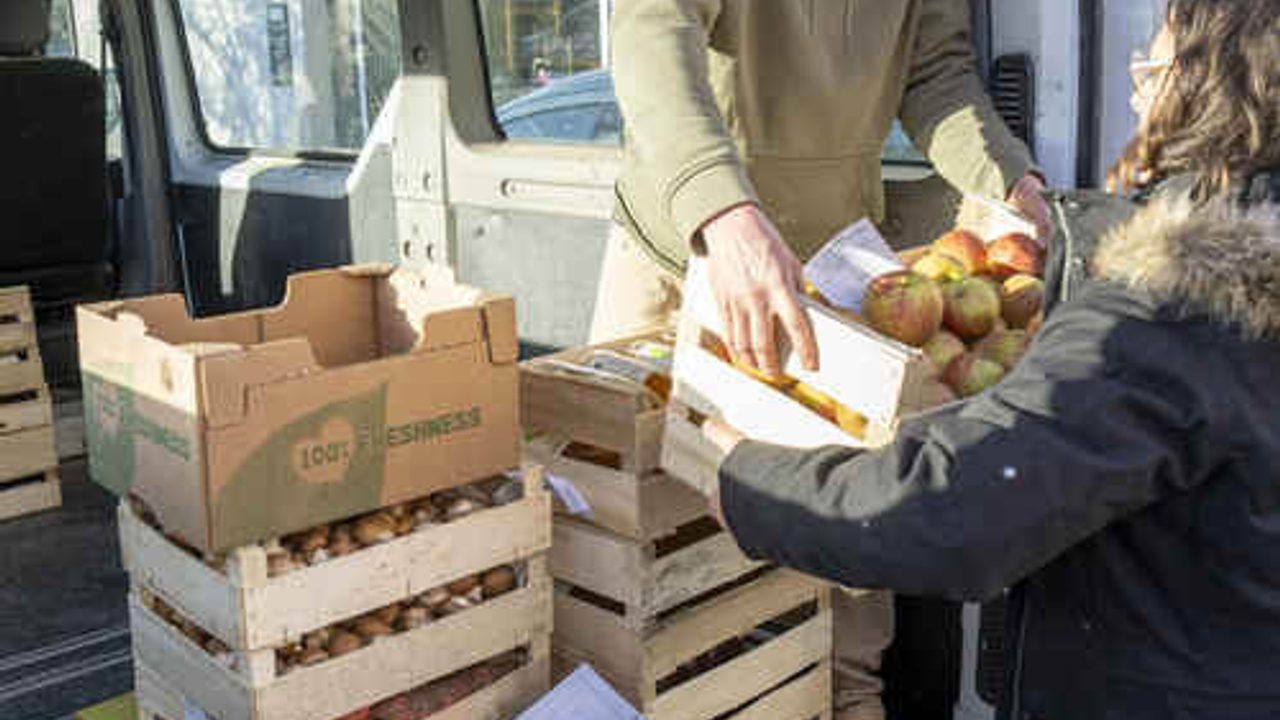 Une personne donne une cagette de pommes à une autre personne, épicerie solidaire