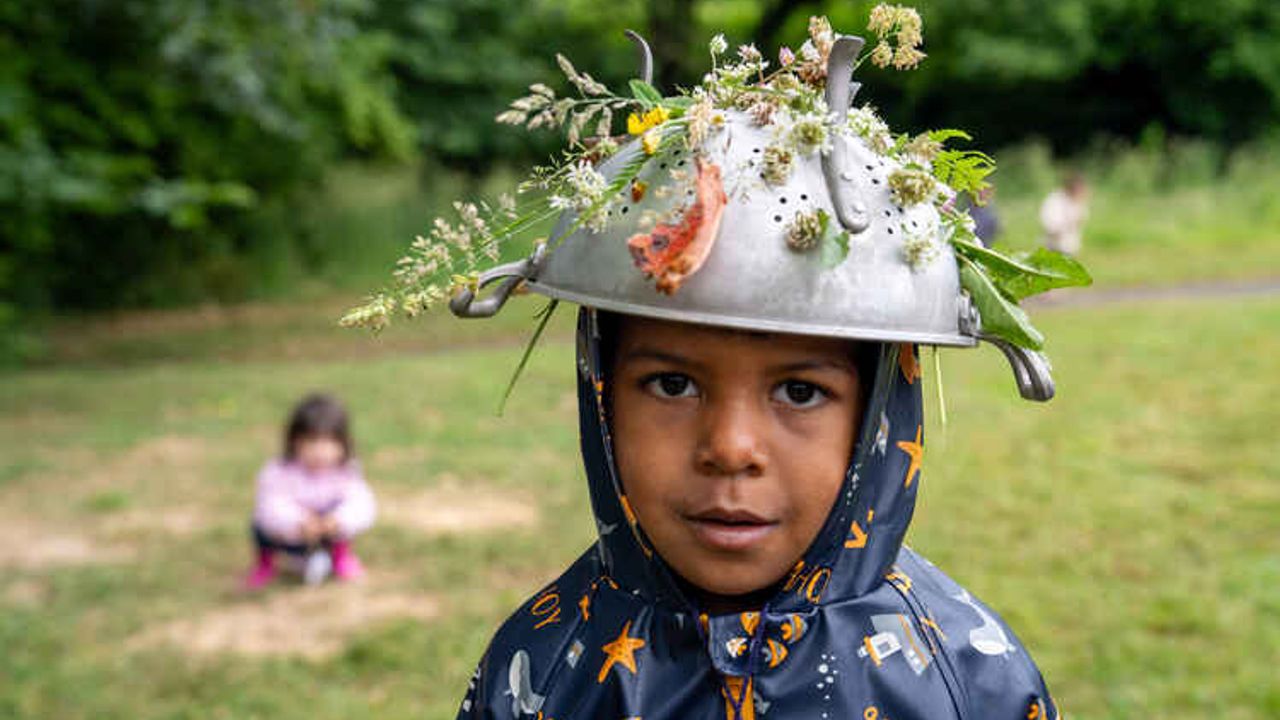 un enfant porte sur sa tête, à la manière d'un casque, une passoire décorée de fleurs
