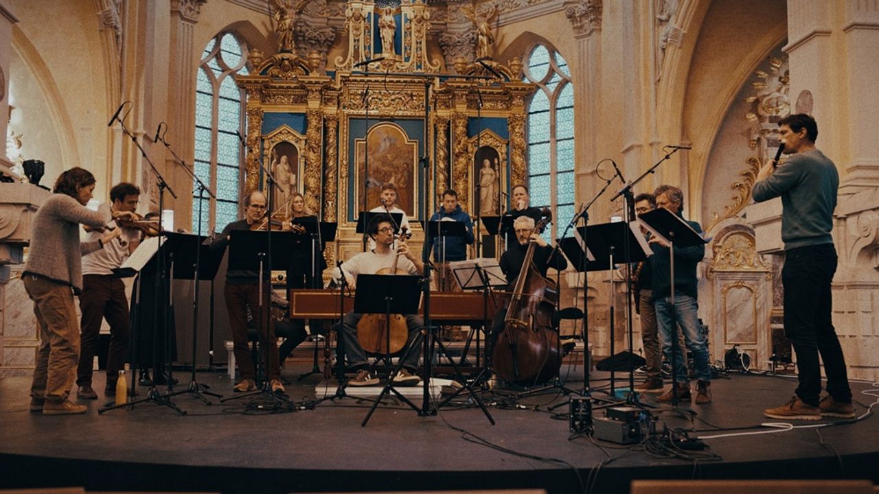 Au premier plan, des musiciens en demis-cercle de part et d'autre d'un violoncelliste, dans un décor somptueux.