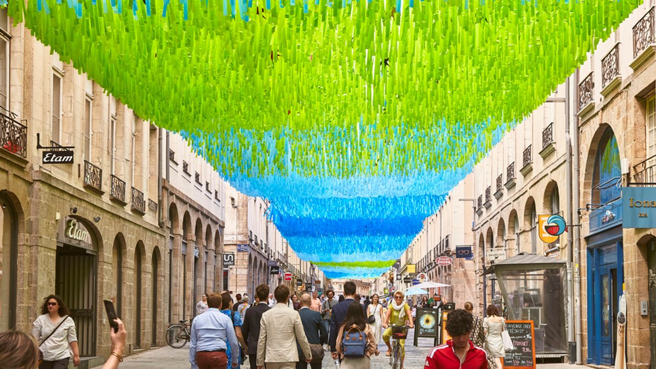 Rue Le Bastard, des habitants se promènent sous un ciel de lanières bleues et vertes.
