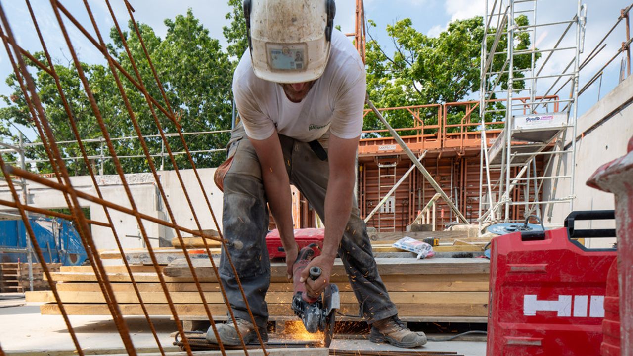 Une personne du BTP en train de scier des câbles métalliques.