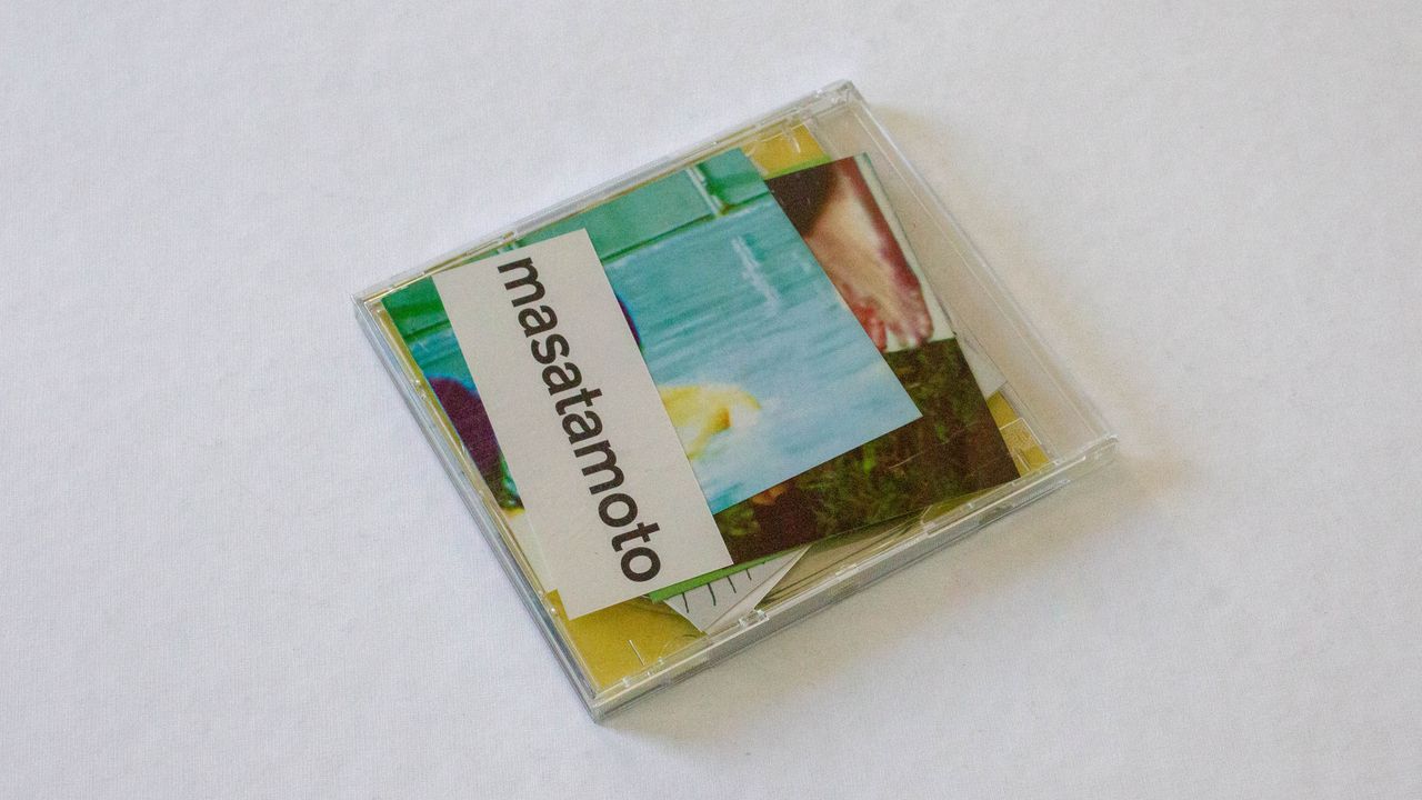 Boitier de cd transparent dans lequel a été glissé plusieurs papiers imprimés. On voit que tous présentent des photos sauf le papier présent contre le boitier : on y lit écrit en noir sur blanc, le mot "masatamoto"