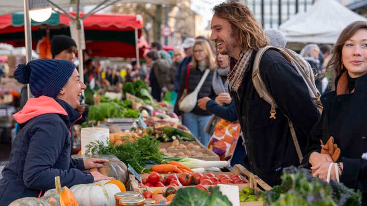 Une commerçante et un client souriants sur le marché des lices.