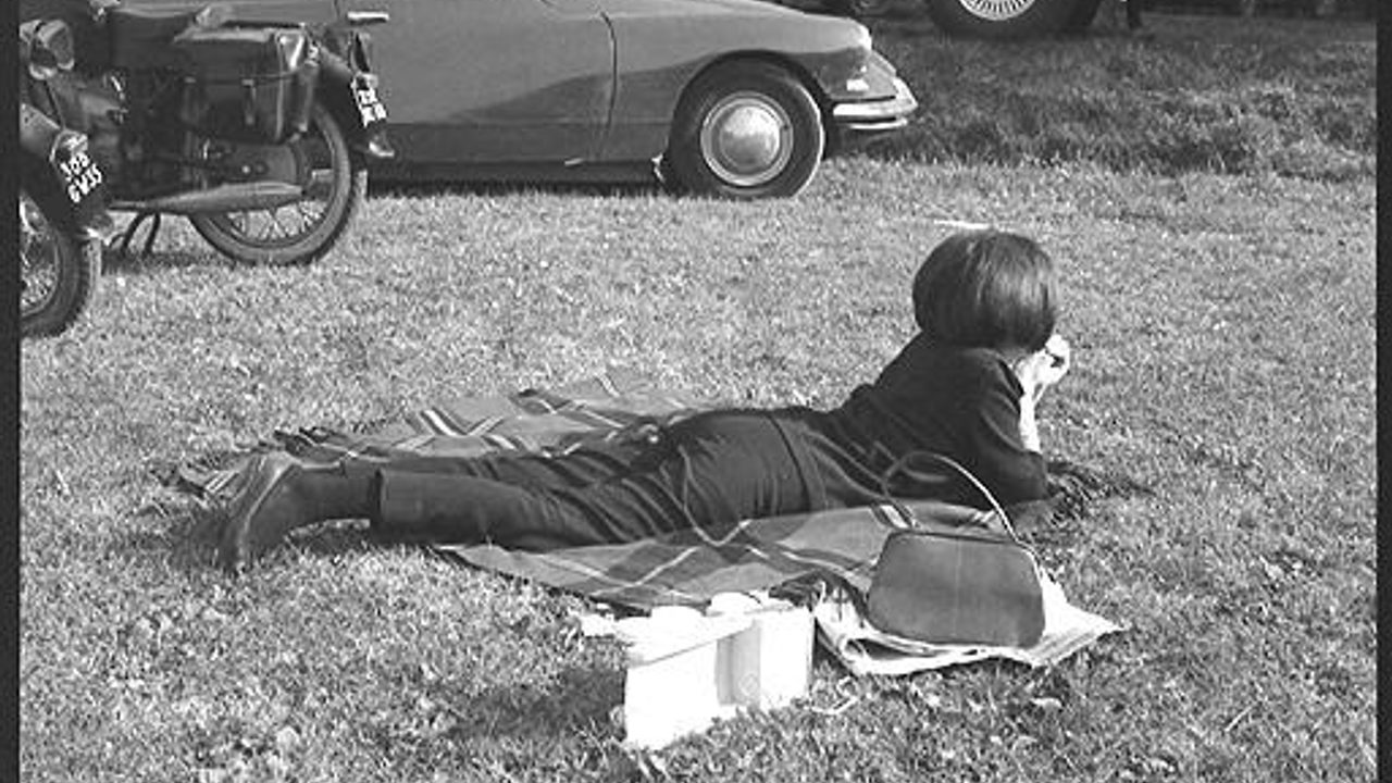 Photo d'un jour de match, une personne est allongée dans l'herbe devant une moto, une voiture et un bus.