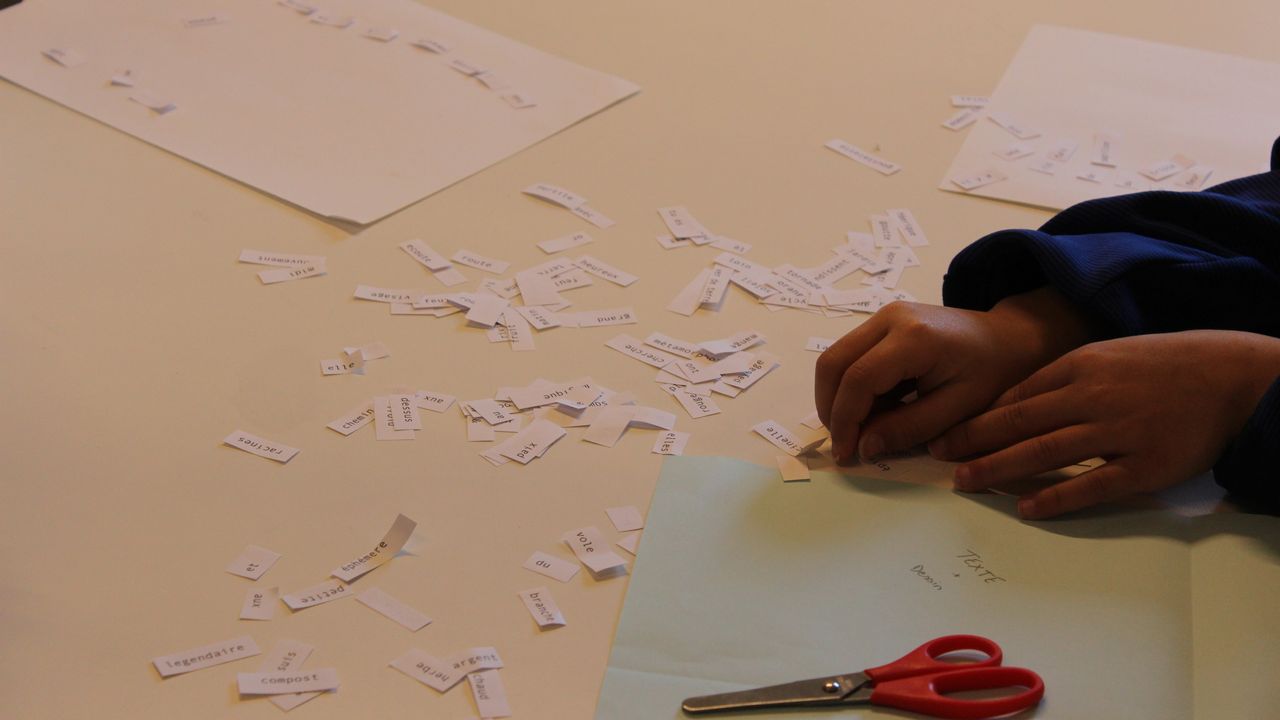 Des mains d'enfant assemblent les mots découpés éparpillés sur une table