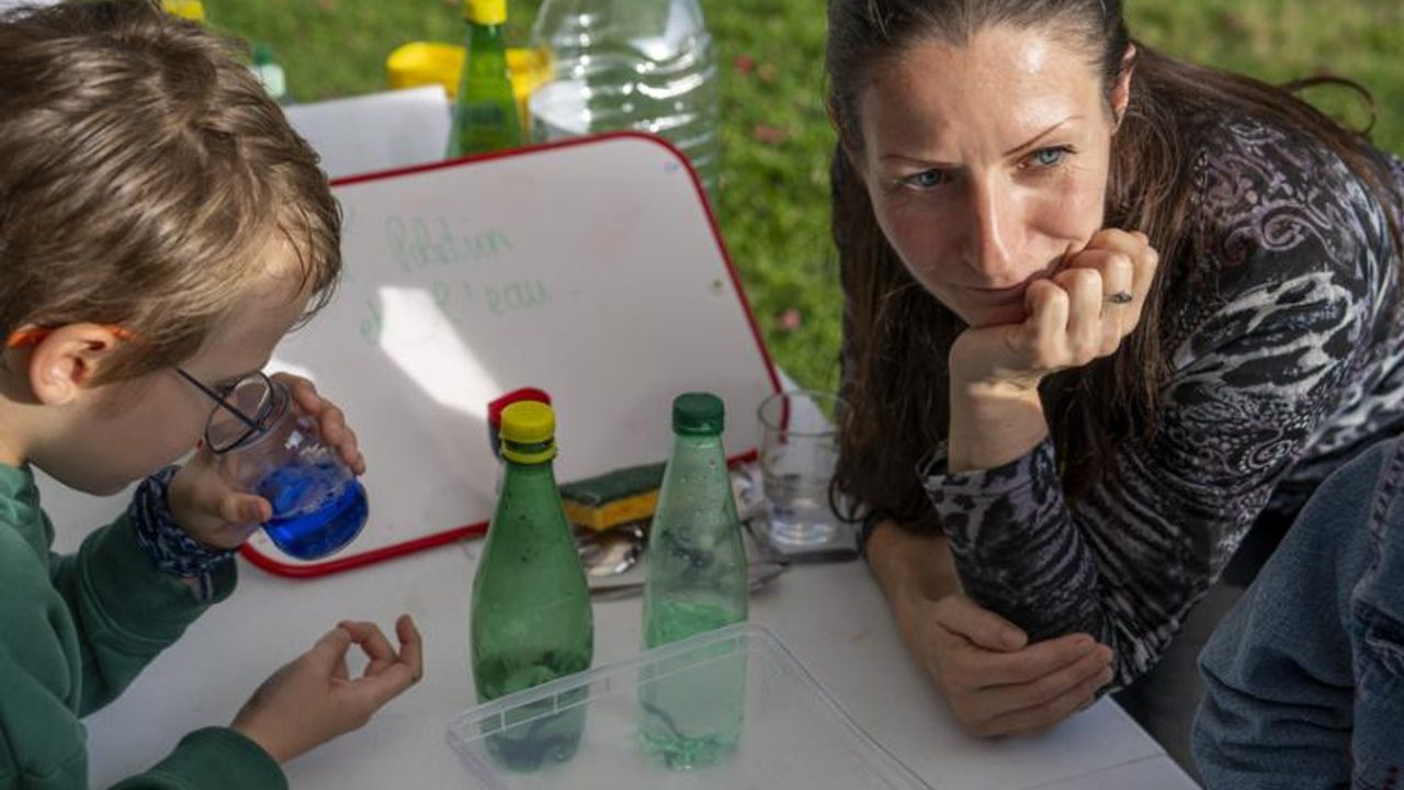 Un enfant manipule une fiole colorée dehors à côté d'une animatrice