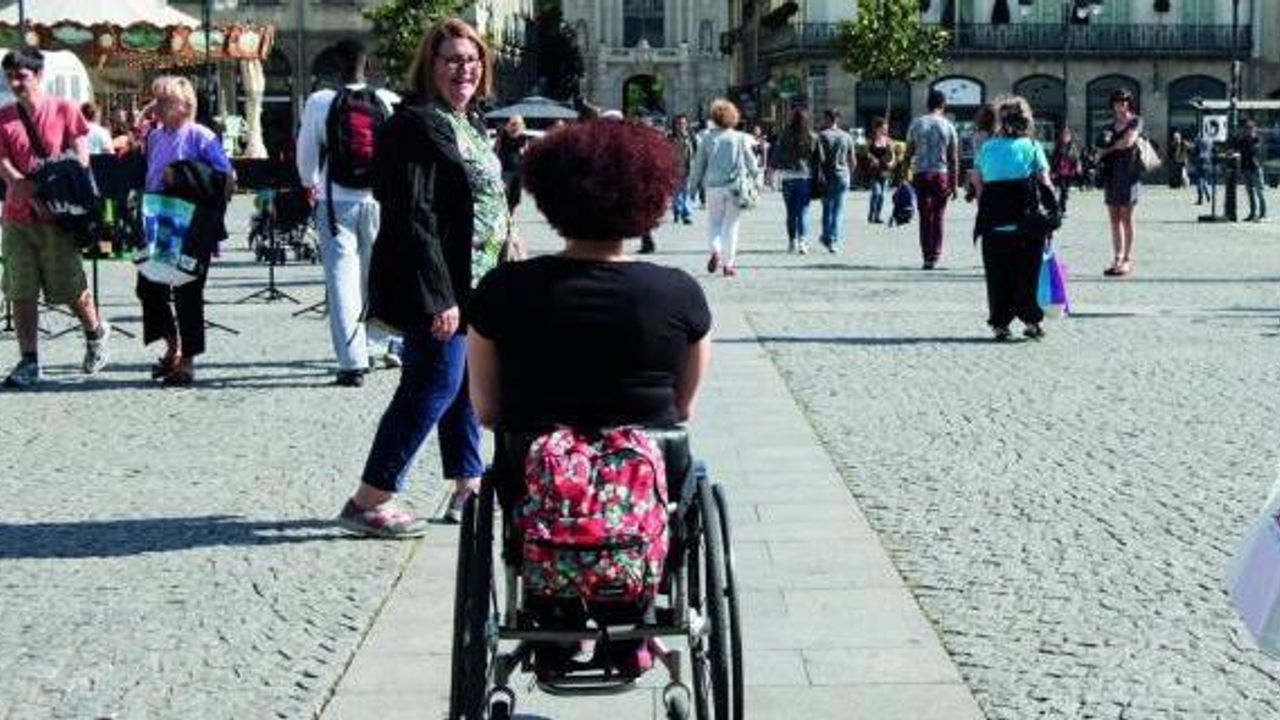 Personne en fauteuil roulant sur une voie dallée au milieu des pavés