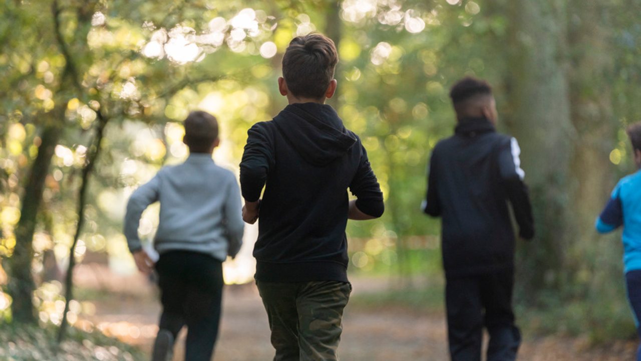 Des jeunes vus de dos en train de courir dans les bois.