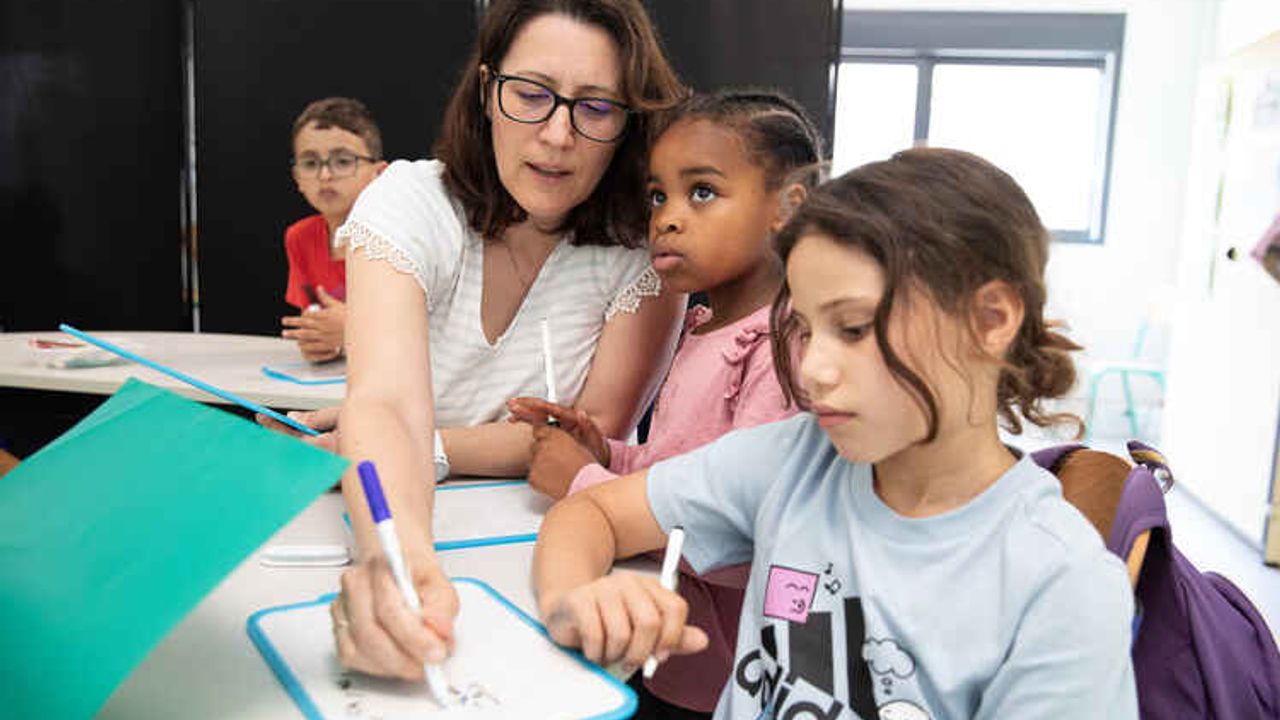 Des élèves révisent des exercices sur une ardois accompagné aux côtés d'une enseignante