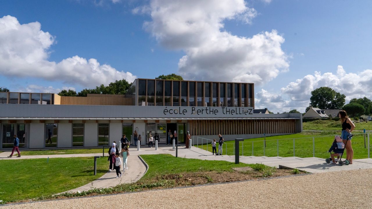 Des personnes vont et viennent sur le parvis herboré d'un nouvel établissement scolaire