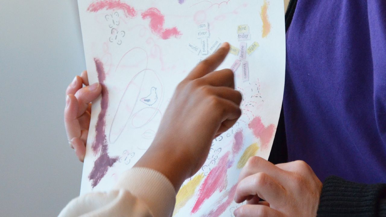 L'artiste Margaux Janisset montre un dessin qu'elle a réalisé aux élèves de CE2 de l'école Jean Moulin. Une des enfants désigne du doigt une figure dessinée sur la feuille. 