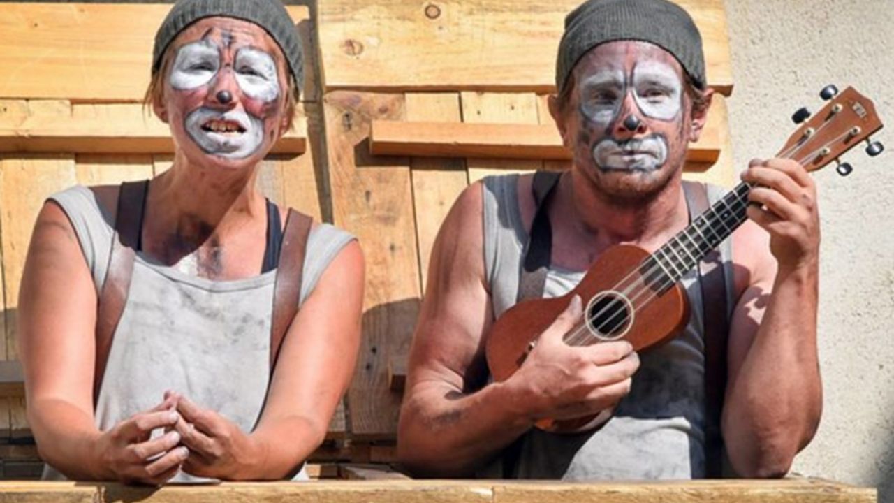 Au premier plan, deux clowns maquillés , dont un tient une guitare minuscule
