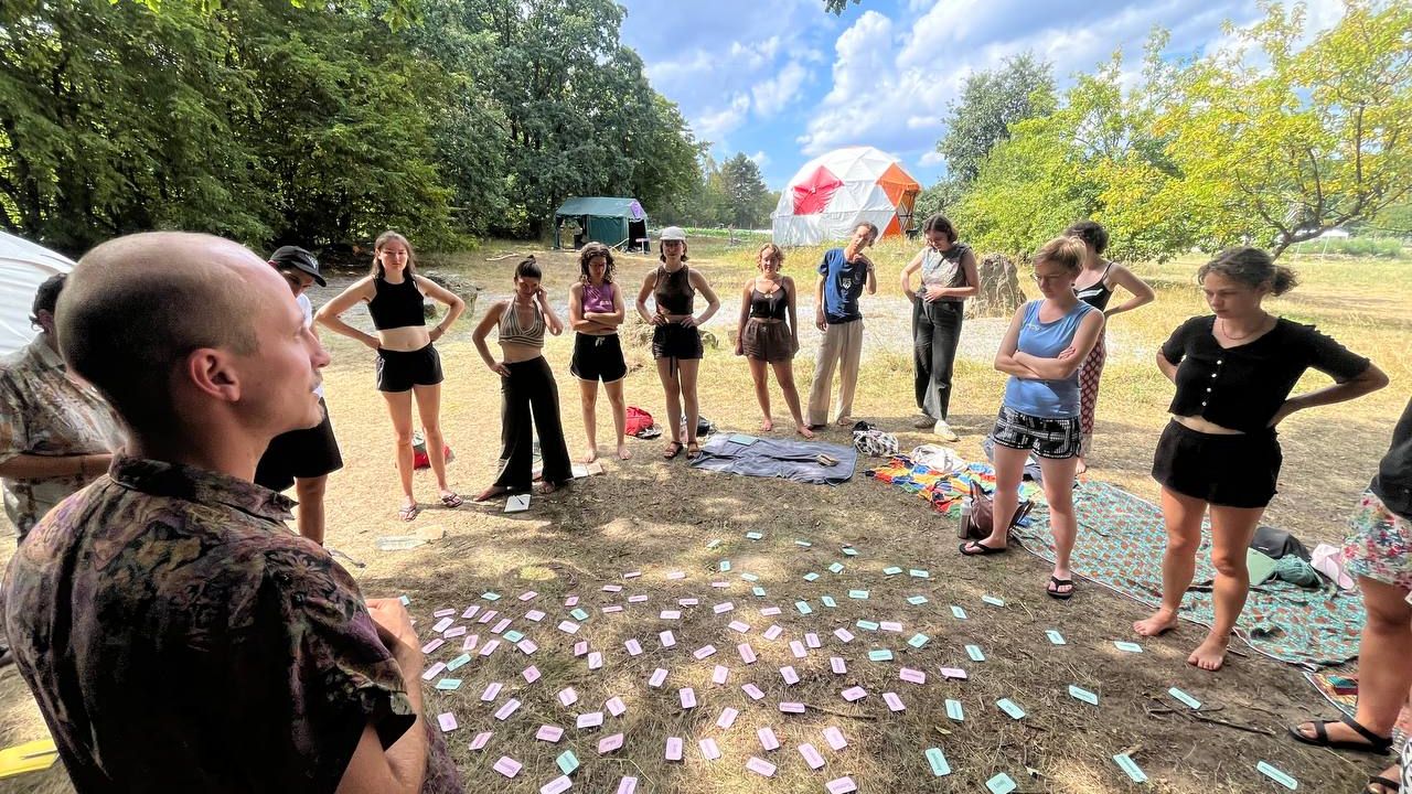 People standing outside in a circle at a workshop, with pieces of paper on the ground