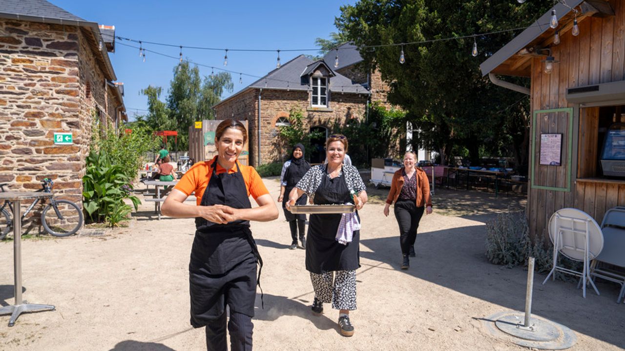 Des personnes marchent dans une cour. L'une d'entre elles porte un plat cuisiné