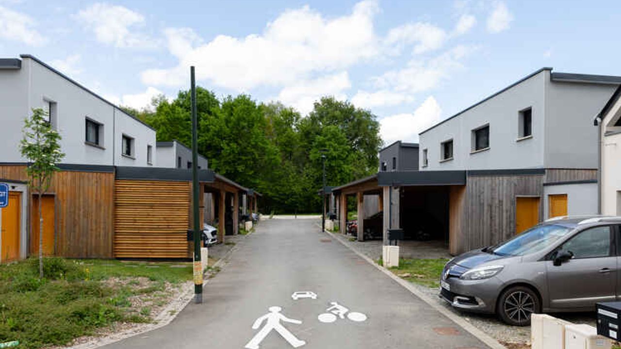 Vue d'une petite rue à Nouvoitou avec, à gauche et à droite, des maisons individuelles mitoyennes récentes d'un étage et, en arrière-plan, des arbres.