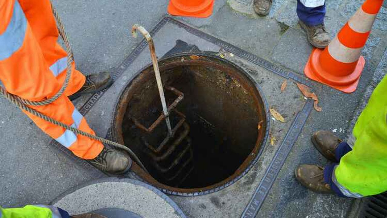 Quatre agents de l'assainissement autour d'une bouche d'égout ouverte.