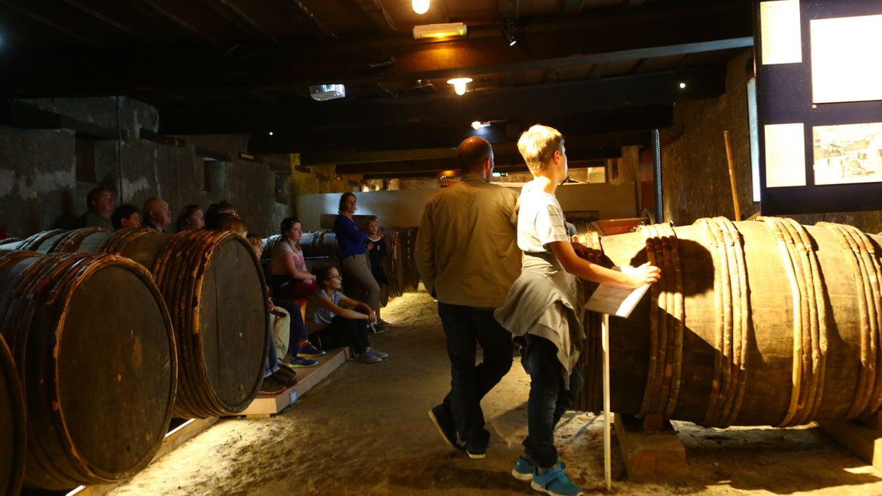 Des gens se tiennent à côté des barriques de cidre dans l'espace d'exposition permanent.
