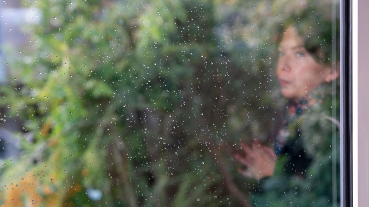 une jeune femme est postée derrière une fenêtre pluvieuse.