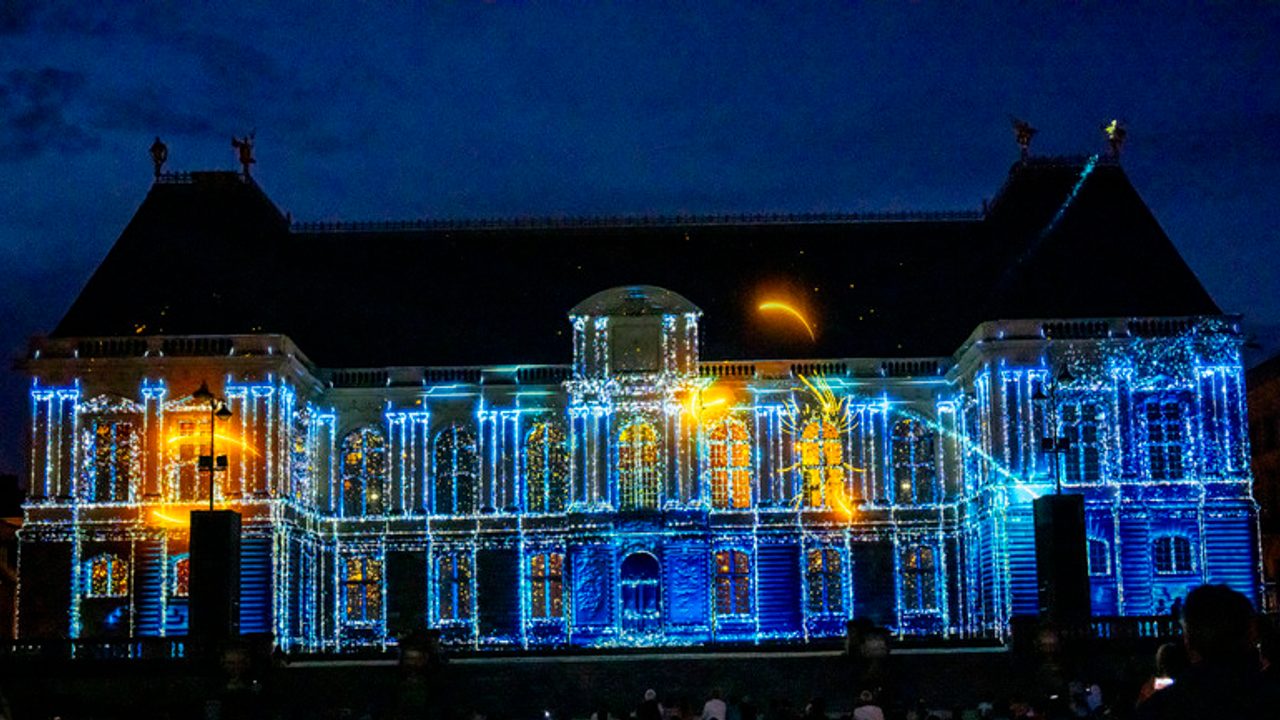 Projection lumineuse sur la façade du Parlement de Rennes un soir d'été, on voit une scène avec des lumières bleues et dorées.