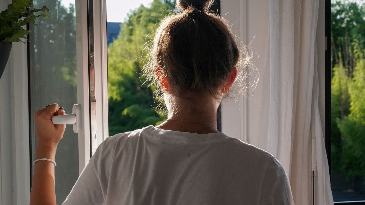 Photo d’une jeune fille dans sa maison, devant une fenêtre ouverte vers un jardin.