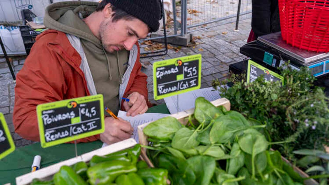 Un homme derrière son étal sur lequel sont disposées des cagettes de légumes avec les étiquettes du dispositif Ici c'est local.