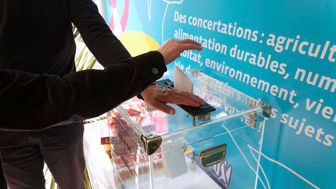 Photo d’un stand de vote du budget participatif à Rennes. Une main met un bulletin dans l'urne.