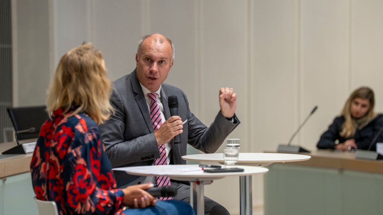 une personne assise répond à une autre personne un micro à la main