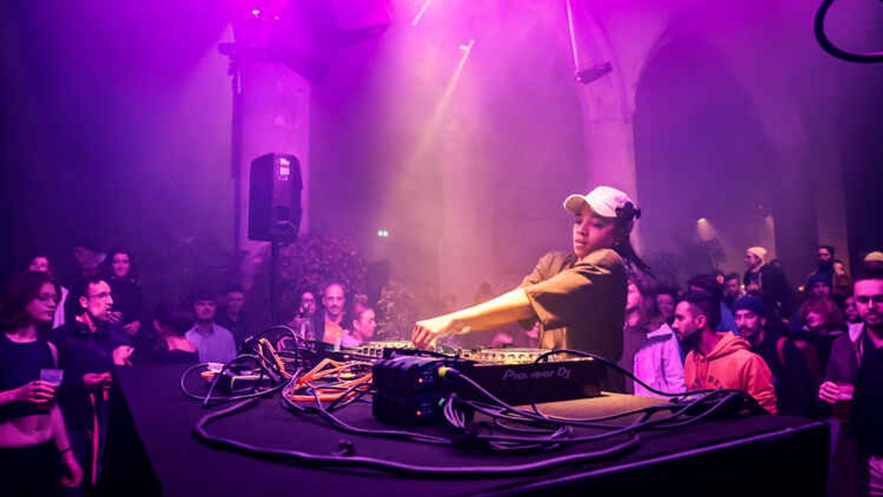 Une jeune femme DJ joue devant un public sur un fond de lumière violette