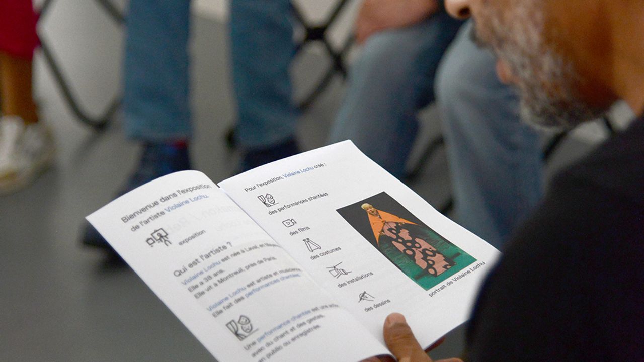 Un visiteur du groupe lie une page du livret FALC.