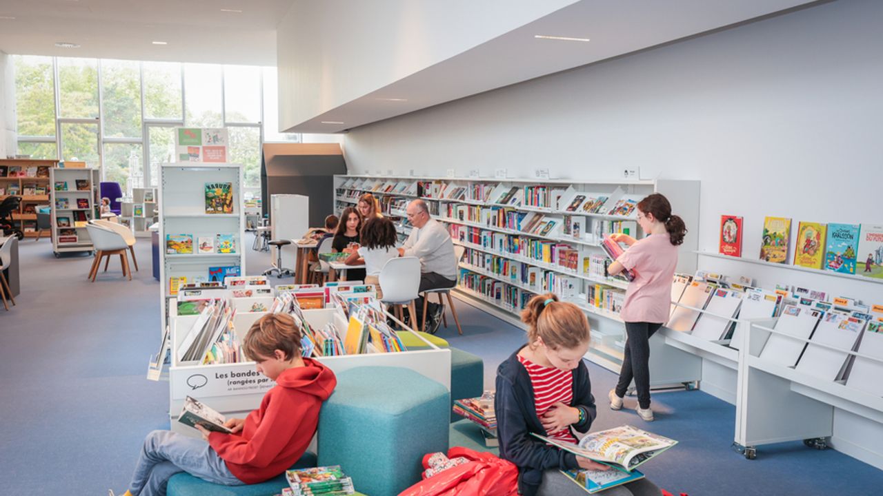 Vue de l’intérieur de la bibliothèque de l’Antipode. Des enfants lisent sur des bancs pendant que d’autres cherchent des livres.