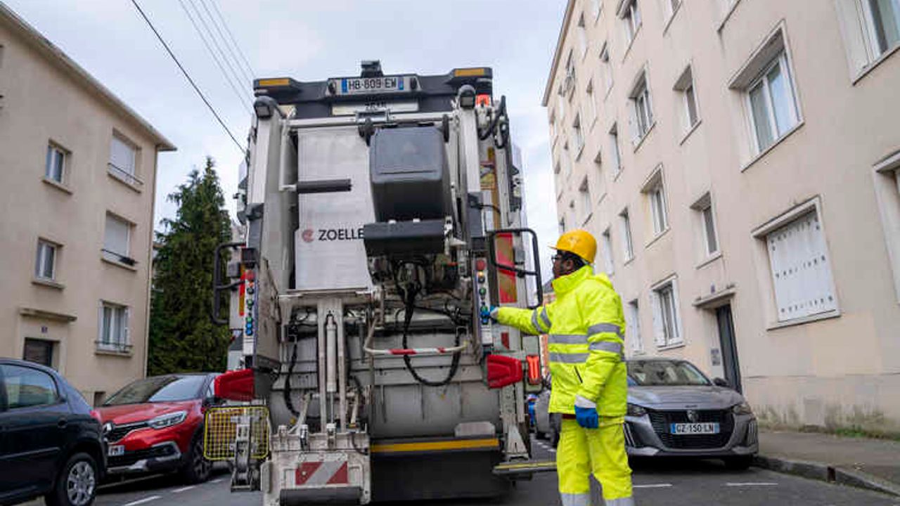 Un éboueur charge une poubelle dans un camion de collecte au pied d’un immemble.