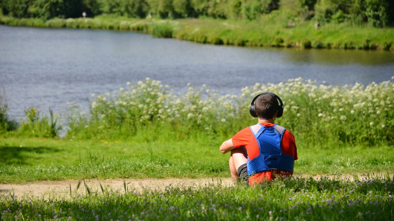 Une personne assise dans l’herbe regarde vers une étendue d’eau.