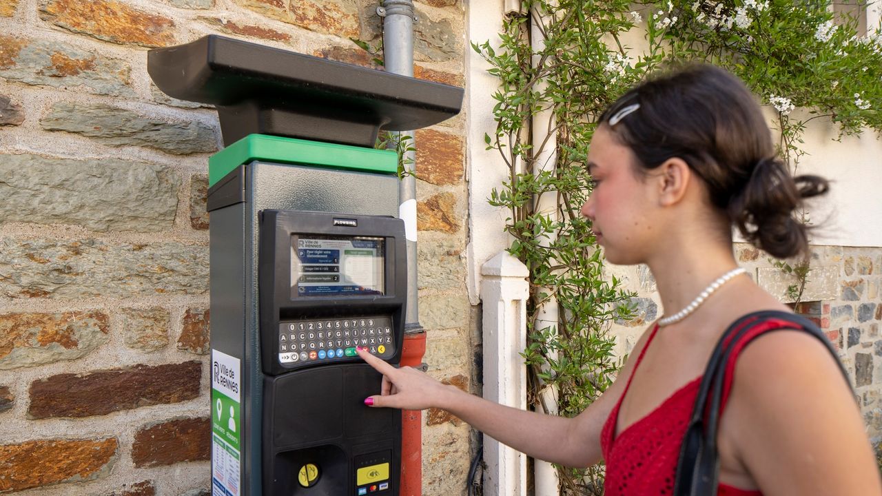 Jeune femme qui règle son stationnement à un horodateur dans une rue de Rennes.