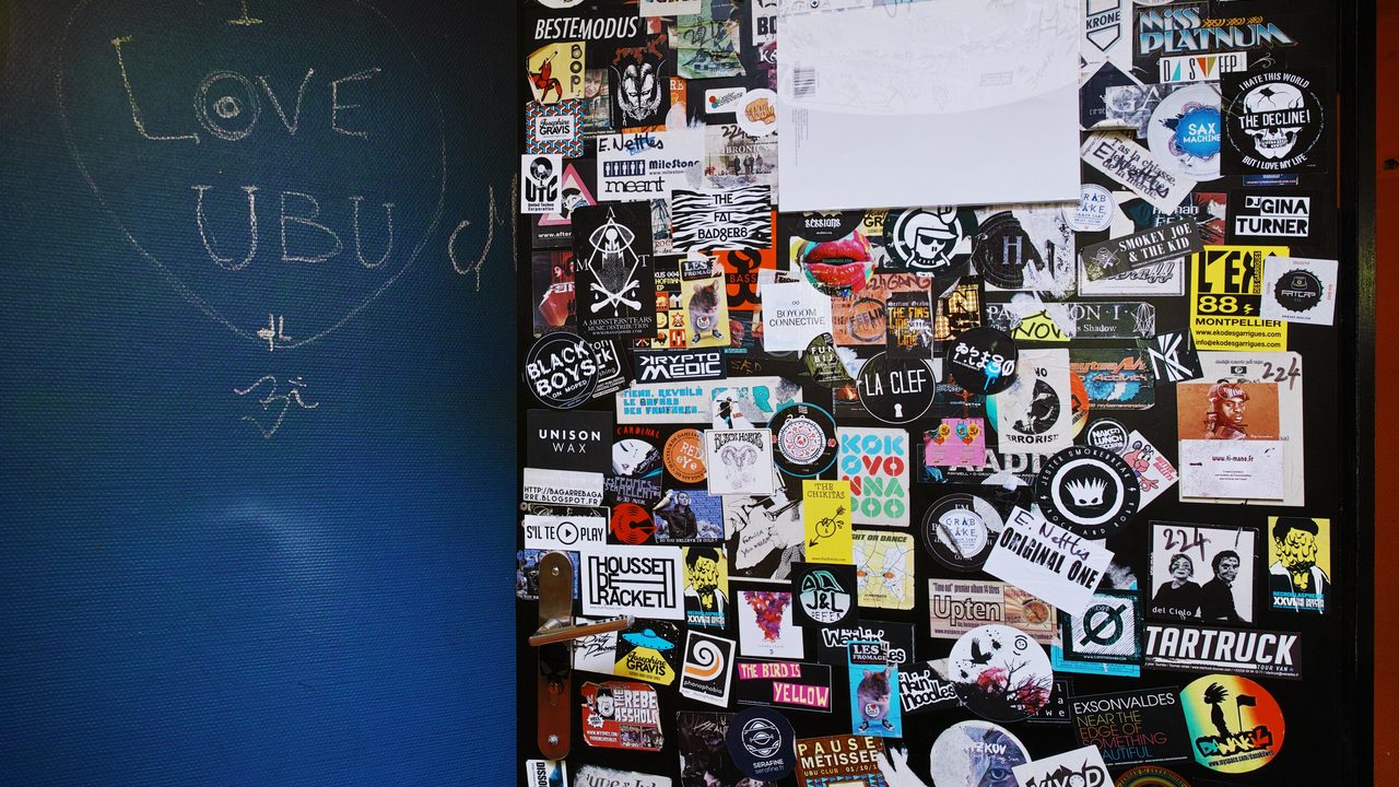 un mur de l'ubu recouvert de stickers de noms de groupes