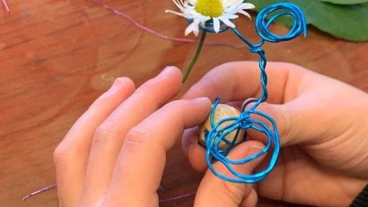 Des mains d'enfant tiennent une structure de fils métalliques surmontée d'une pâquerette.