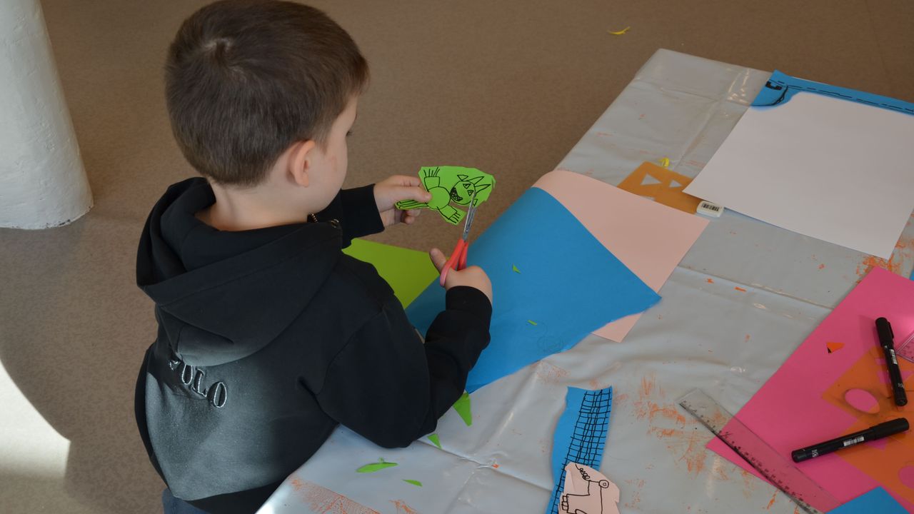 Un enfant découpe les contours de son personnage dessiné sur du papier vert.