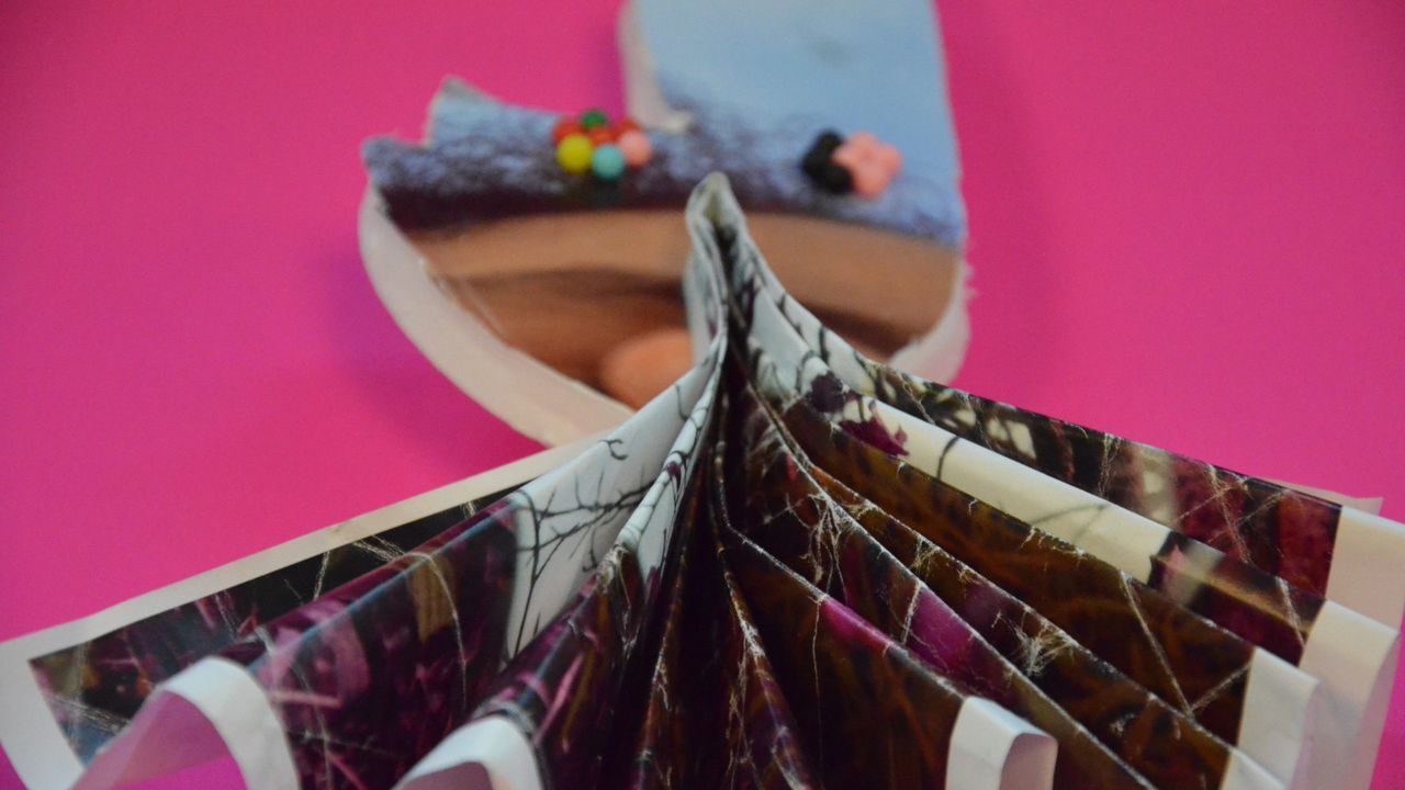 Une photo en éventail est posée sur une forme de polystyrène, elle aussi recouverte d'une photo d'une élève. L'œuvre est posée sur un papier rose fuschia.