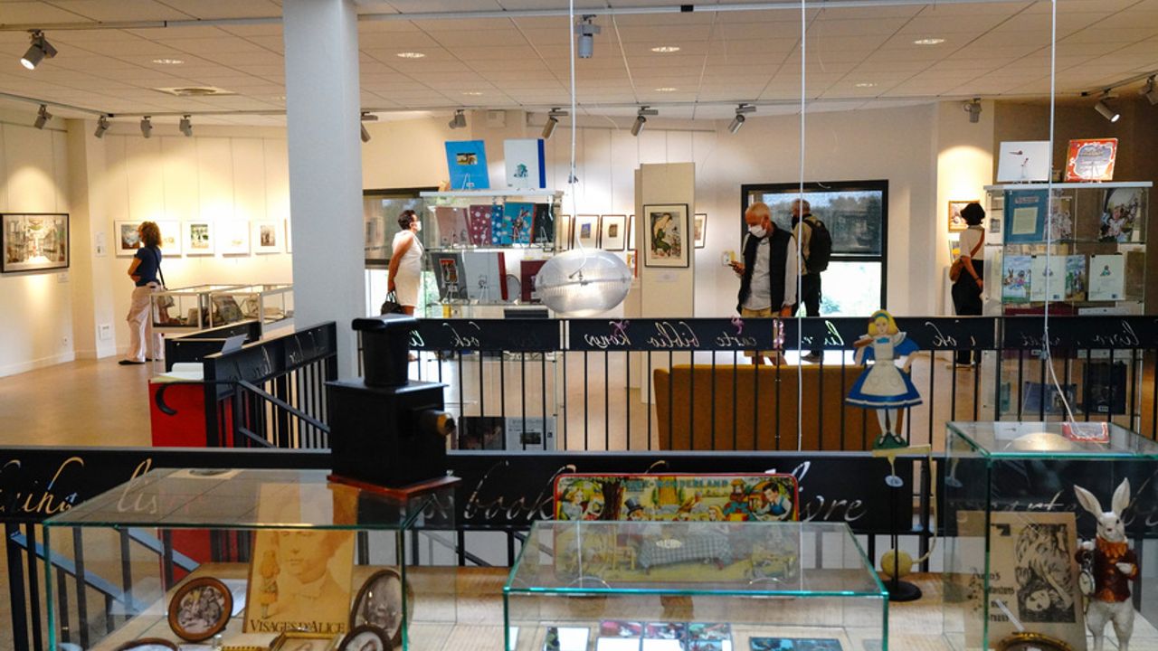 Au premier plan, vitrines contenant des cadres photos. En arrière-plan, une exposition visitée par le public.