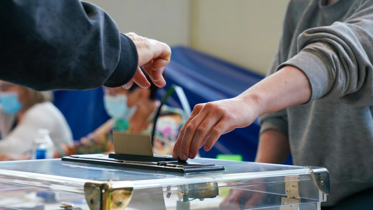 Une personne glisse une enveloppe de vote dans une urne.
