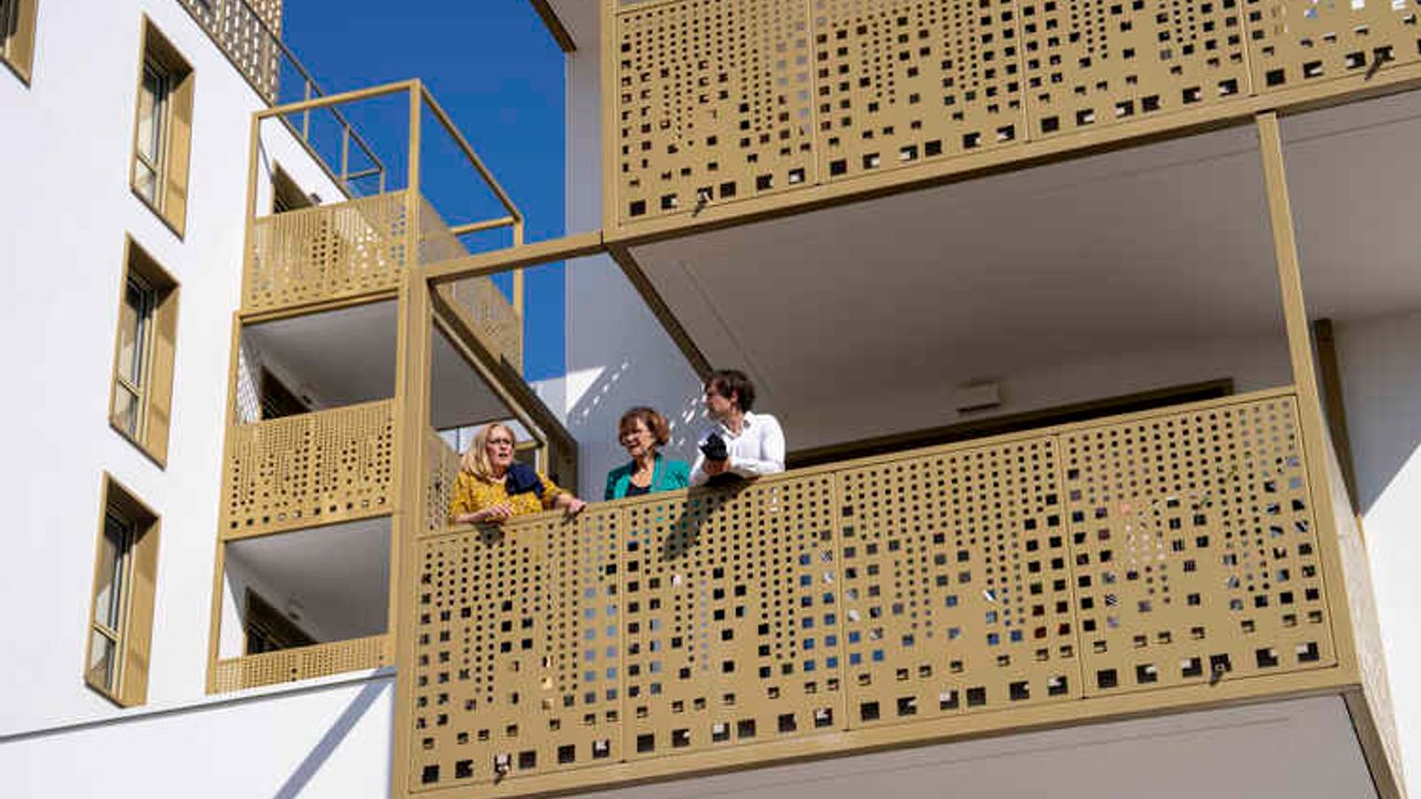 trois femmes sont accoudées au balcon d'un immeuble récemment construit
