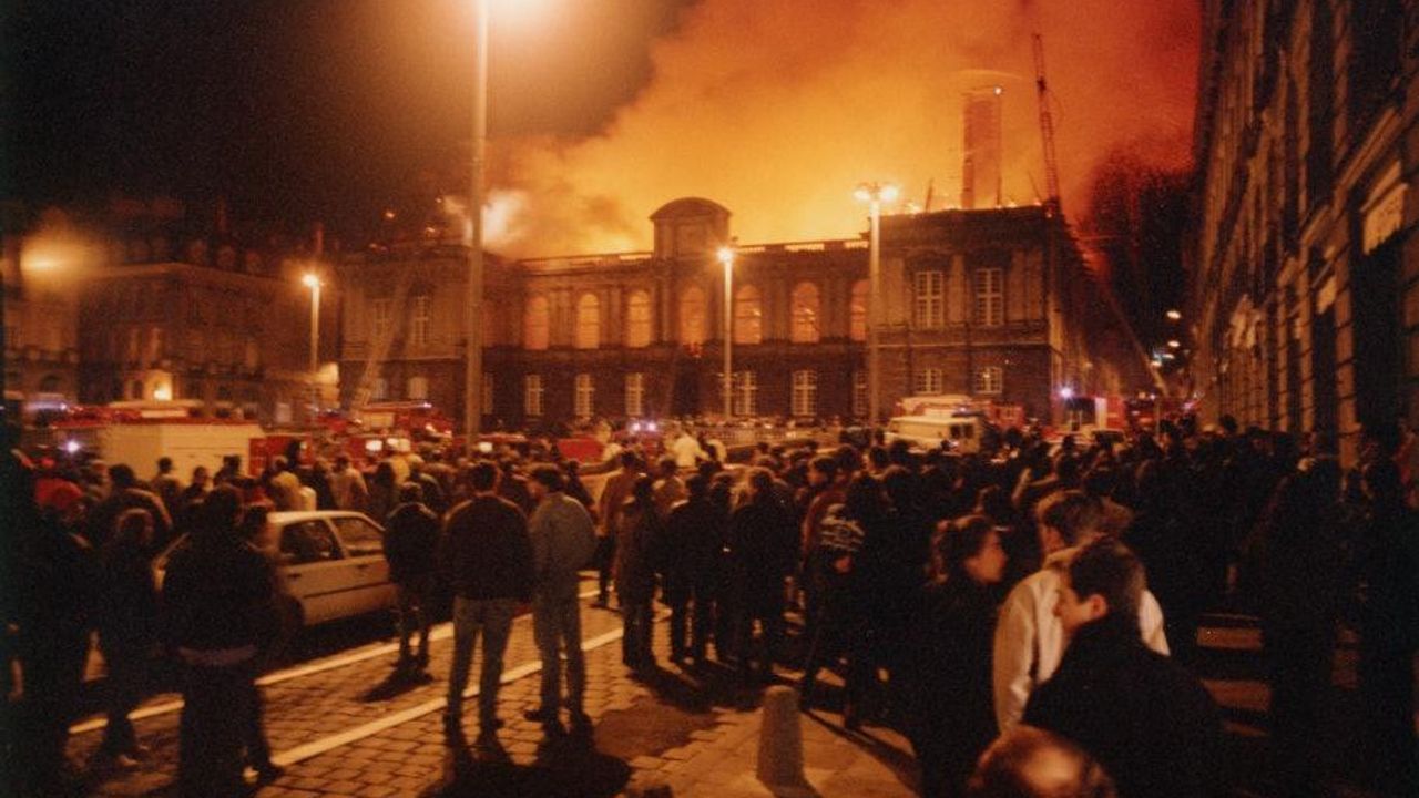 Une foule de gens se regroupe de nuit devant le parlement en feu. 