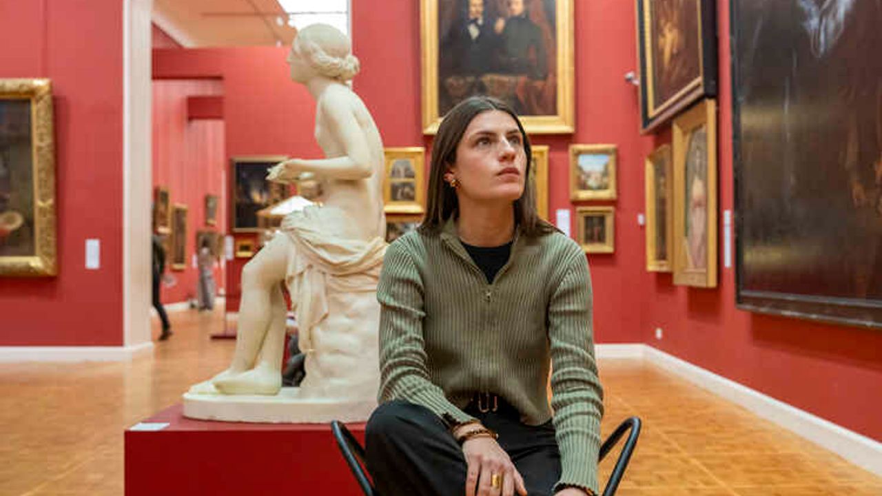 Jeune femme regardant une oeuvre assise devant une statue