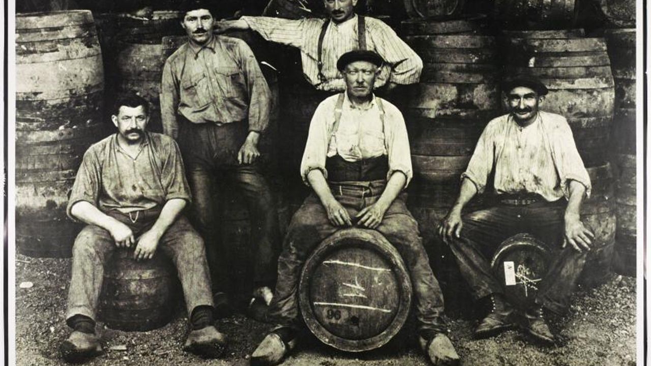 Photo en noir et blanc : cinq hommes prennent la pose devant ou sur des fûts.