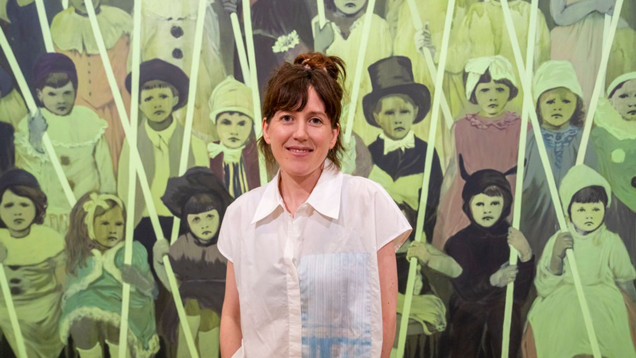 Claire Tabouret porte une chemise blanche devant une de ses oeuvres représentant des enfants.