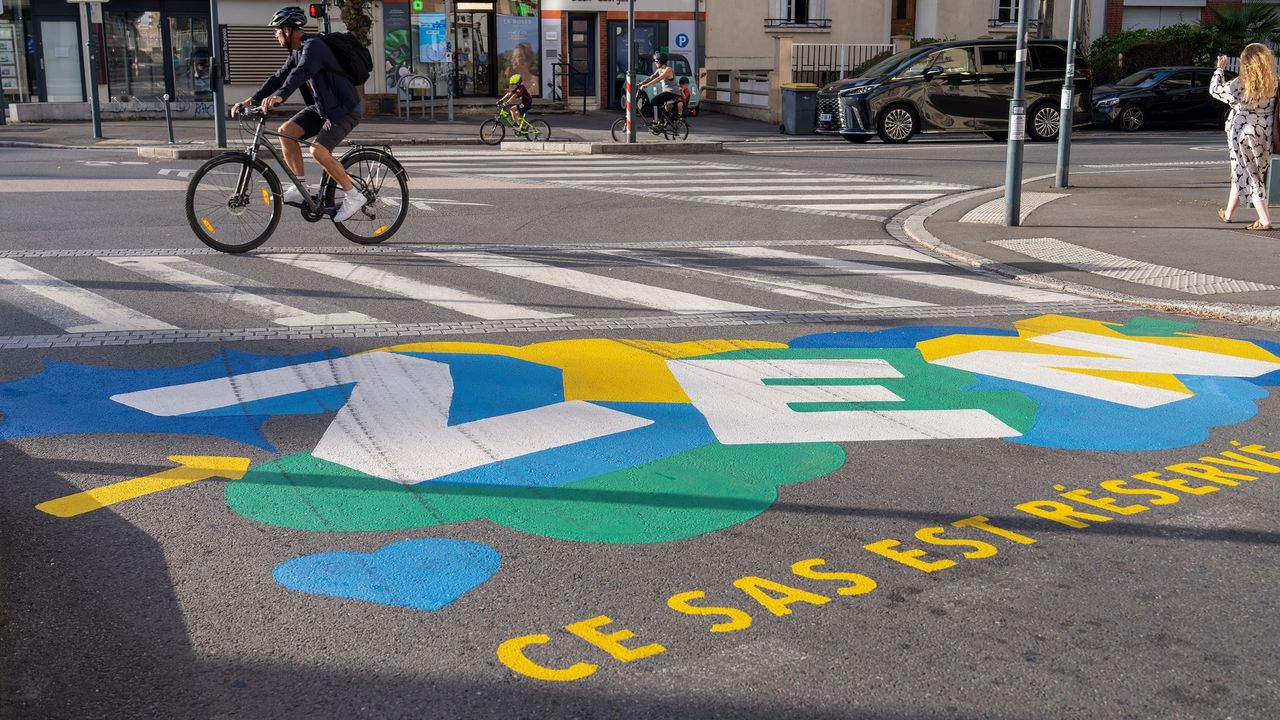 San vélo au niveau d'un carrefour, en arrière plan un cycliste passe.